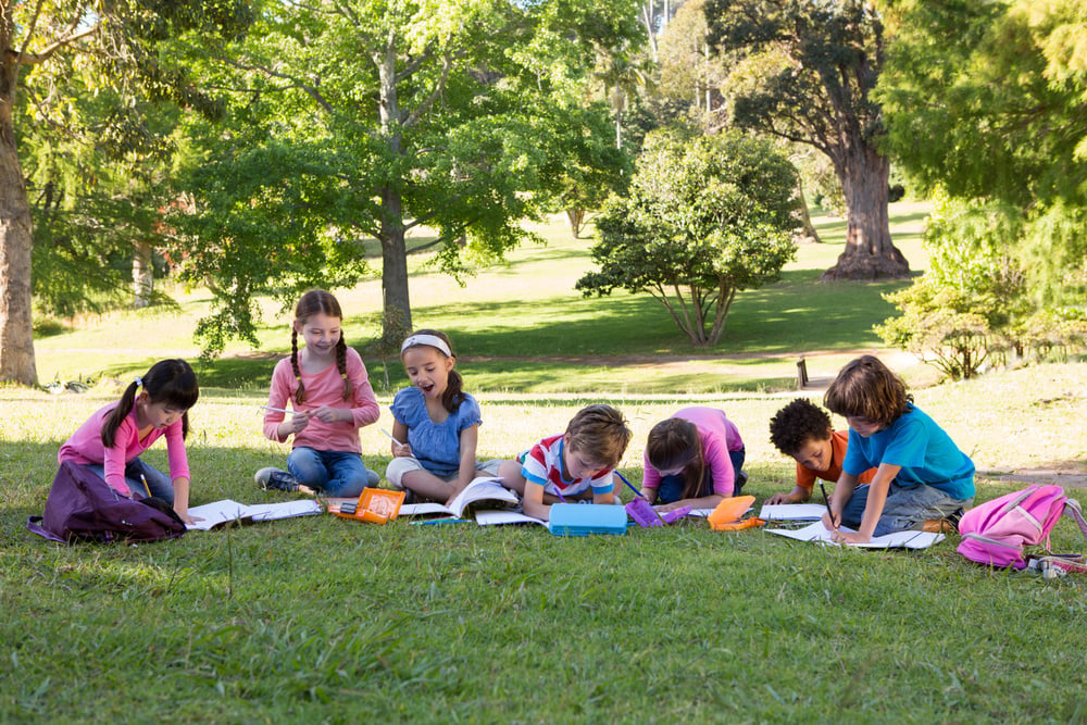 School children doing homework on grass on a sunny day